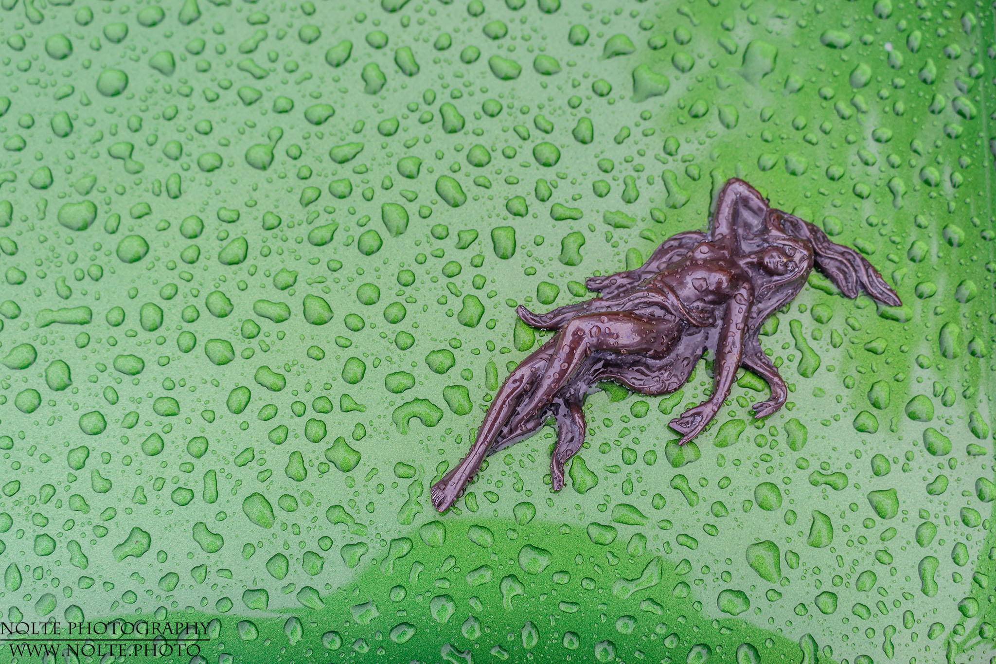 Eine kleine Frauenskulptur auf Nassem Fahrzeuglack